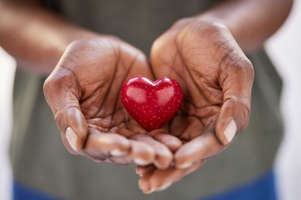 Two hands gently holding a small red heart close up